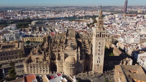 Aerial drone footage of the gothic cathedral in Seville old town with its famous Giralda bell tower, an ancient minaret, in Andalusia, Spain. Shot with a tilt up motion. 