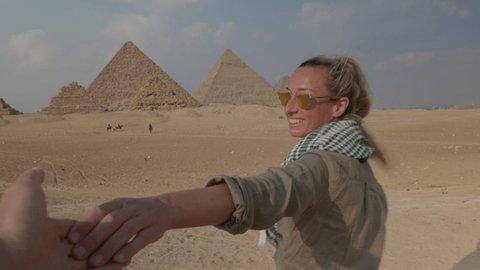 Follow me concept: Young woman holding companion hand, leading him towards the Great Pyramids of Giza. People travelling adventure concept. 
