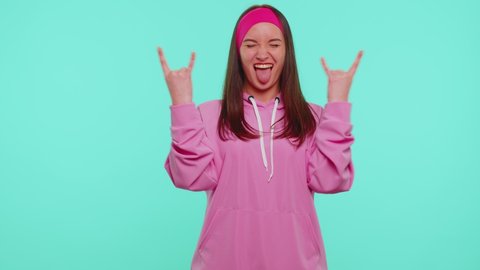 Rock-n-roll! Overjoyed delighted sincere teen girl 20s years old in pink hoodie showing gesture by hands, cool sign, shouting yeah with crazy expression, dancing, emotionally rejoicing in success win
