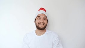 Caucasian handsome man in red Santa hat on white background smiles and waves his head in different directions. Christmas joy and emotions. Celebrate New year. Minimalism. 4K footage.