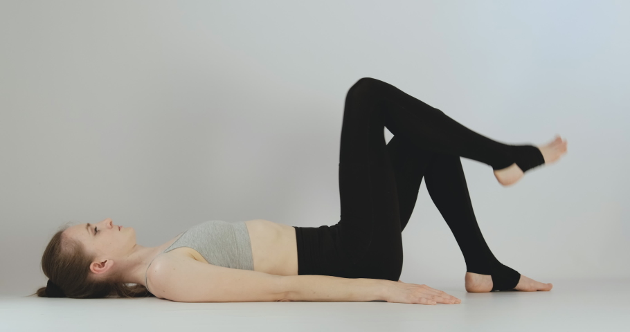 Girl lies on her back and pulls her knees to her chest. Practicing yoga. Young woman does exercises to develop flexibility.