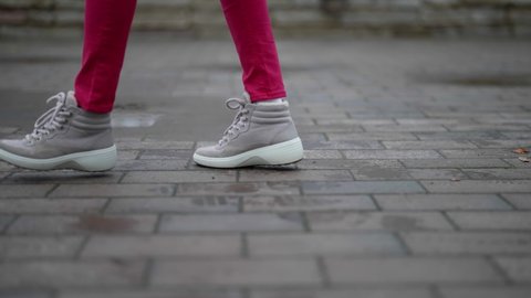 Close-up of a woman legs while walking along the road happily jumping through puddles. A woman in sneakers is walking down the street. Confident legs of a girl walking through the city.