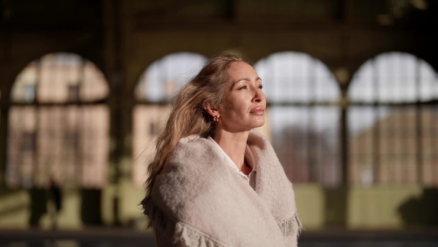 Portrait of an adult attractive woman standing at the railway station. An open portrait of a happy tourist having a good time waiting for a train.
