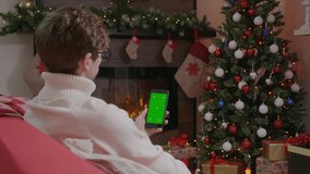 Handsome Man holding smartphone with Green Screen on Christmas background with gifts. Mobile Phone with Chroma Key.