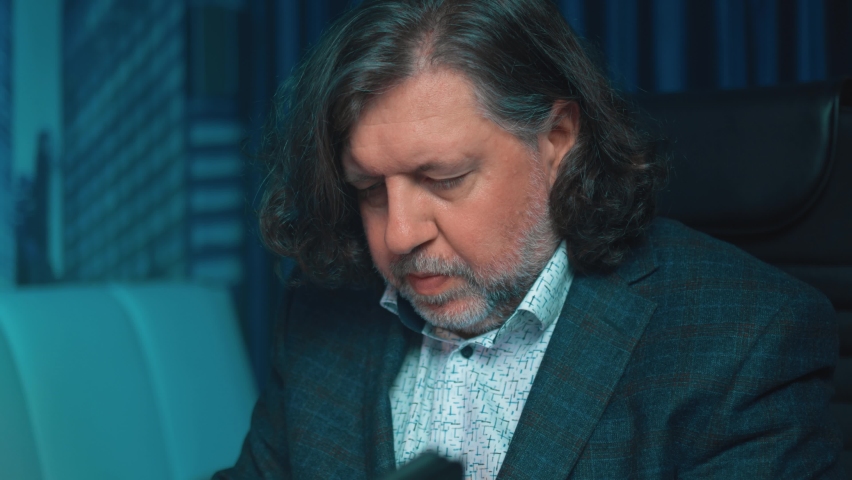 Portrait of a business man in a home office in the evening. He is talking on his cell phone with suppliers. Remote work during the pandemic. Communication via smartphone.