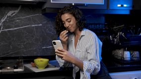 happy woman video chatting in modern kitchen snacking