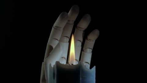 Closeup shot of a burning candle rotating with a mannequin hand behind it. Religion concept. Dark blue candle. Creepy candlelight. Studio shot. Black background.