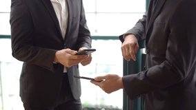 Cropped view of two smart businessmen in a black suits standing on the office corridor using mobile phone to make a contact online by scanning qr code from the other for adding friend on social media. - Powered by Shutterstock - Get 15% off with code: PIKWIZARD15
