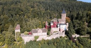 Aerial orbit of Zwingenberg Castle surrounded by a lush forest on a sunny day.