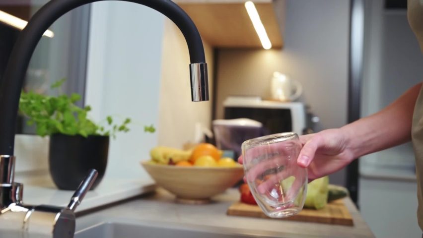 Woman pouring water from faucet into glass at the kitchen