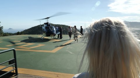 Blonde young girl Boarding a landed Helicopter on helipad. Touristic helicopter tour to Christ the Redeemer statue on the top of Sugarloaf, Rio de Janeiro, Brazil. Cristo Redentor on Corcovado.