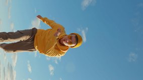 Happy Young man caucasian runs fast amusingly moving his hands with his legs with making funny faces on his face social media wearing yellow hoodie beanie sunglasses close up blue sky summer Lifestyle