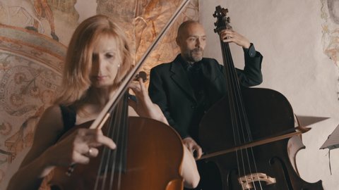 Low angle shot of a male and female cellist playing in a string quartet in a medieval style setting