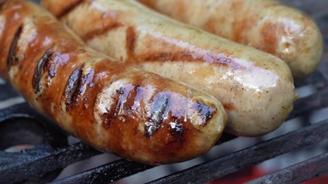 Extreme closeup of sausages on the grill with smoke and fire and fat running down.