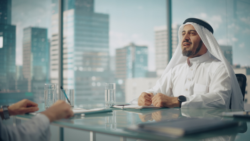 Smiling Emirati Businessman in White Traditional Outfit Sitting in Office with Business Partners. Shake Hands on Successful Investment. Saudi, Emirati, Arab Businessman Concept. Royalty-Free Stock Footage #1082792089