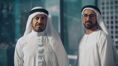 Portrait of Two Successful Muslim Businessmen in Traditional Outfits Gently Smiling, Wearing White Kandura and Black Agal Keeping a Ghutra in Place. Saudi, Emirati, Arab Businessman Concept.