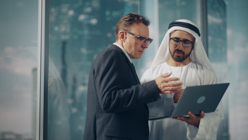International Operations Manager Meeting Saudi Business Partner in Traditional Kandura. They're Standing in Modern Office, Using Laptop Computer. Successful Saudi, Emirati, Arab Businessman Concept. | Shutterstock HD Video #1082792170