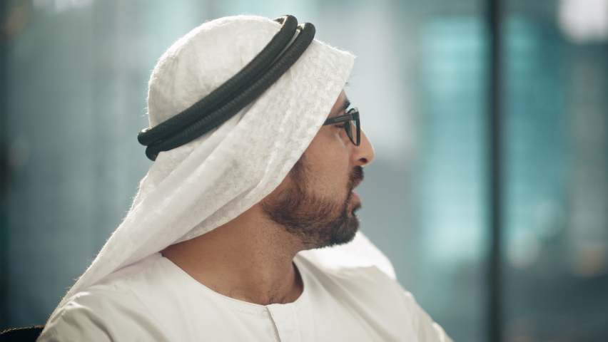 Portrait of Successful Arab Businessman in Traditional Outfit Gently Smiling, Wearing Glasses, White Kandura and Black Agal Keeping a Ghutra in Place. Saudi, Emirati, Arab Businessman Concept.
