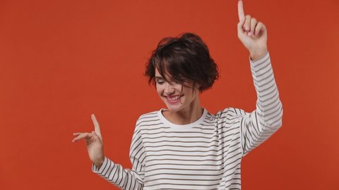 Slow motion fancy vivid bright young brunette woman 20s years old wear striped shirt dance fool around have fun gesticulating with hands enjoy relax isolated on plain orange background studio portrait