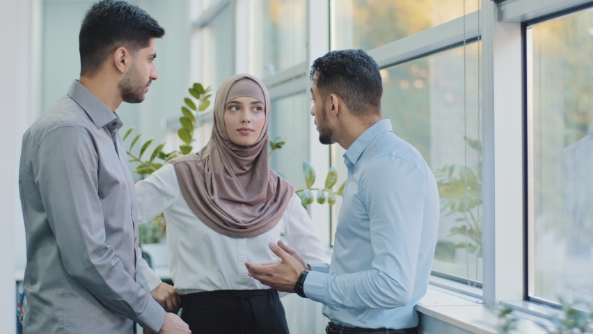 Diverse friends multiethnic colleagues arab muslim woman in hijab and two Indian men chatting, friendly people enjoying pleasant conversation at break, man telling story feeling happy and satisfied Royalty-Free Stock Footage #1082799949