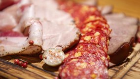 Stock food video of sliced meat snacks for beer party in bar. Salchichon and chorizo sausages, ham and beef slices served on rustic wooden plate in restaurant