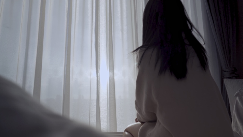 Asian woman wakes up and  open window curtains stretching arms on the bed in the morning, look out the window with city street traffic view, high rise condo apartment, start the day with energy Royalty-Free Stock Footage #1082804938