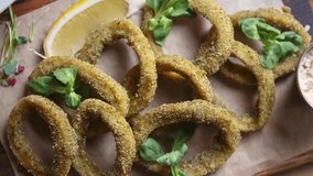 Stock food video of deep fried squid rings cooked for beer snack in bar and served on rustic wooden plate and parchment paper, filmed directly from above in 4k ultra hd