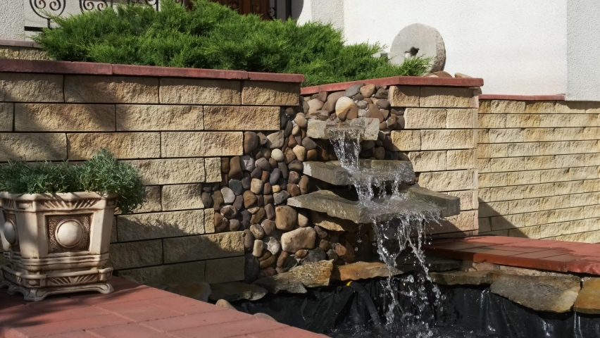 A beautiful decorative small waterfall made of stones and slabs in the back or front yard of the house.