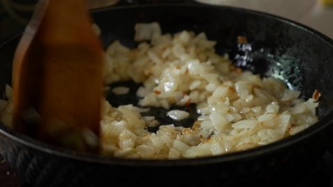 Frying onions in a pan with oil. Stir onion in skillet with wooden spatula.
