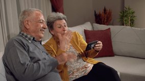 Old age and happy news.
Elderly couple making a video call with their grandchildren on the phone. Grandfather and grandmother who are longing for their children. Sadness, Happiness, Joy.