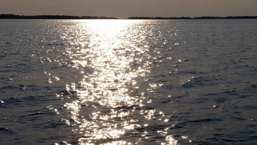 Slow motion travel over lake with bright reflections from the sun. Horizon with silhouetted trees in the distance. Lake Nipissing, Ontario, Canada.