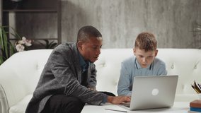 Black male English teacher explains educative materials on laptop computer to concentrated boy student during private lesson at home slow motion