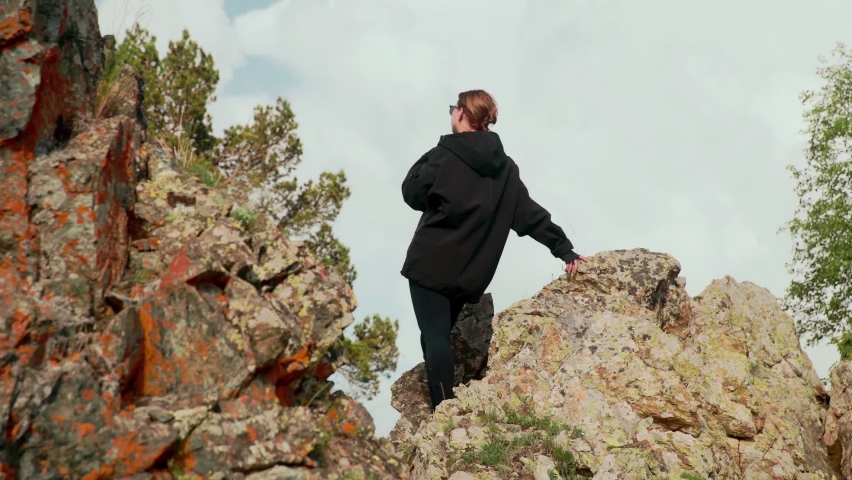A rear view of a girl sitting on rocks in the mountains and looking into the distance. Tourism
