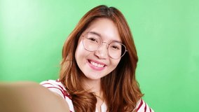 The portrait of a selfie Asian woman with eyeglasses is smiling with laughter being positive emotions on video call online. Green screen