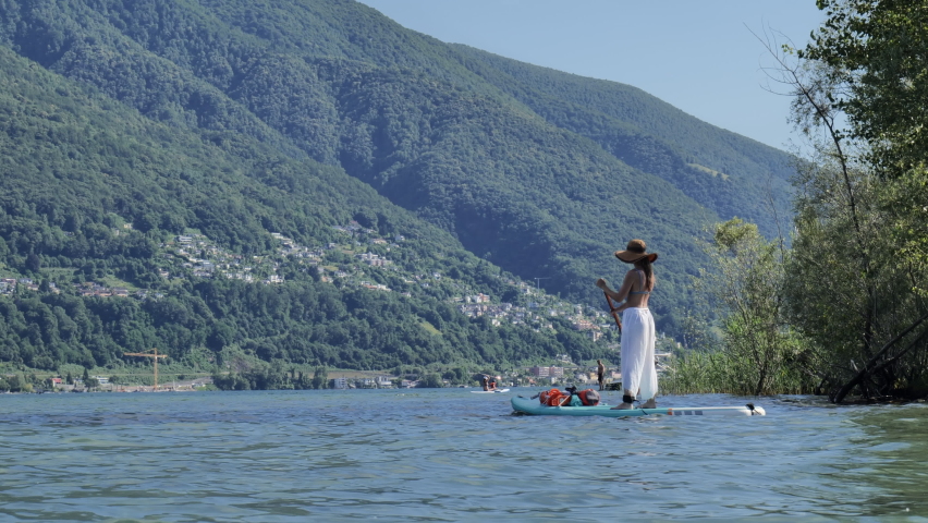 Young sportive woman on a stand up paddle board rowing on calm lake waters in summer. Female enjoying a free day on the lake 