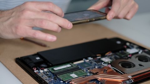 Unrecognizable engineer takes pictures of the laptop motherboard on a smartphone. Electronic renovation, business, occupation concept