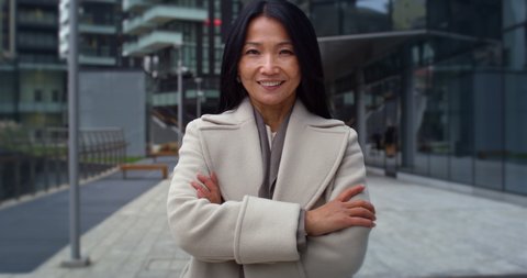 Cinematic shot of happy mature asian business woman is smiling in camera satisfied with her job in busy city center by the way to office before to start her work day.