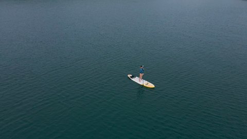 Aerial shot. Young women is having fun. Stand Up Paddling in the sea. SUP. Red hair girl Training on Paddle Board among rocks