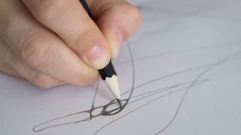Close-up of a pencil in hand which draws lines on a sheet of paper. Designer work on paper using a pencil. The artist draws a sketch on paper. Neurography and therapy.