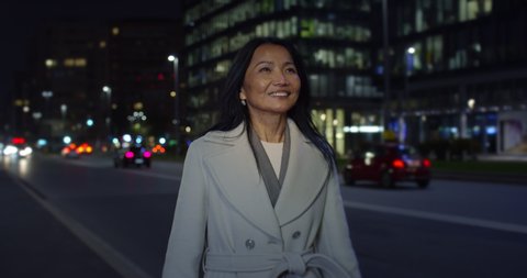 Cinematic shot of happy confident mature asian business woman is smiling satisfied with her job while walking in busy city center after finishing work day at evening.