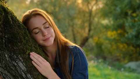 Redheaded woman hugging tre in nature
