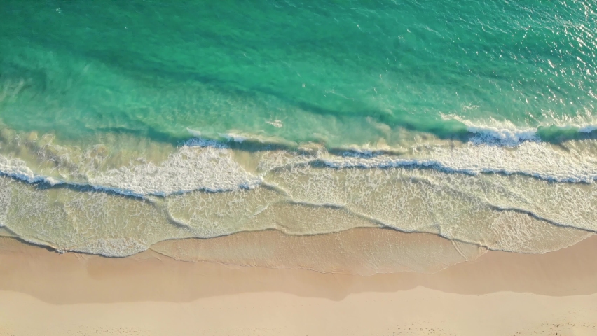 Aerial Top view of a transparent blue sea with beautiful waves at sunny day in summer. Tropical landscape from the air of ocean with azure water, sandy bottom at sunset. Aerial view of sand beach. | Shutterstock HD Video #1082841586
