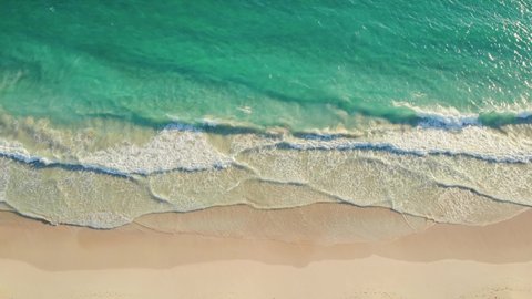 Aerial Top view of a transparent blue sea with beautiful waves at sunny day in summer. Tropical landscape from the air of ocean with azure water, sandy bottom at sunset. Aerial view of sand beach.