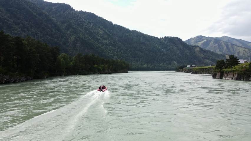 A red inflatable boat sails along the rocky shore
