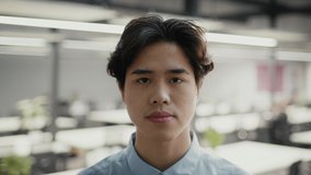 Headshot Of Serious Millennial Asian Businessman Looking At Camera Standing In Office, Wearing Shirt. Business Career And Occupation Concept. Slow Motion