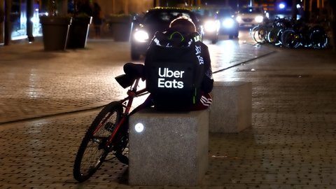 Strasbourg, France - Circa 2019: Cars driving near the Uber Eats delivery man with his bike nearby - and large reflective Uber Eats rucksack backpack