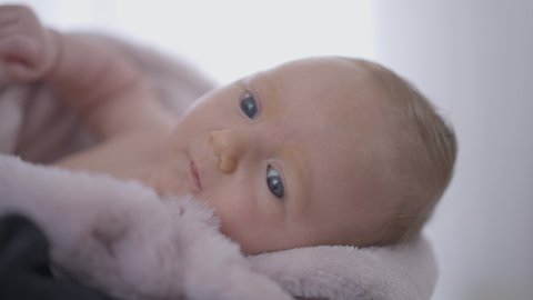 Close-up cute newborn baby girl looking away moving hands. Curios Caucasian child indoors at home. Innocence and lifestyle concept