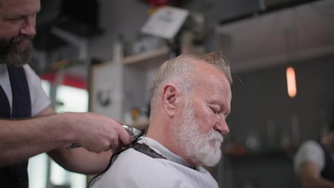 smiling male haircutter does a trimmer for an elderly client with a beard in a barbershop