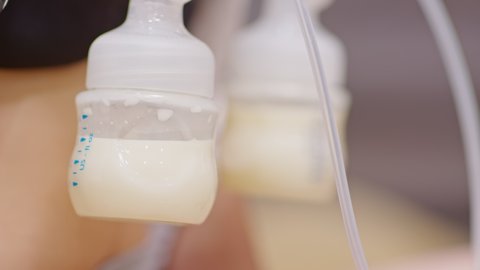 Mother using breast milk pump for baby.Close up Milk from breast pump dropping into milk bottle storage for baby newborn.