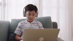 Asian little boy video call online via the internet tutor on a computer laptop with headphone. Homeschooling, Concept online learning at home 